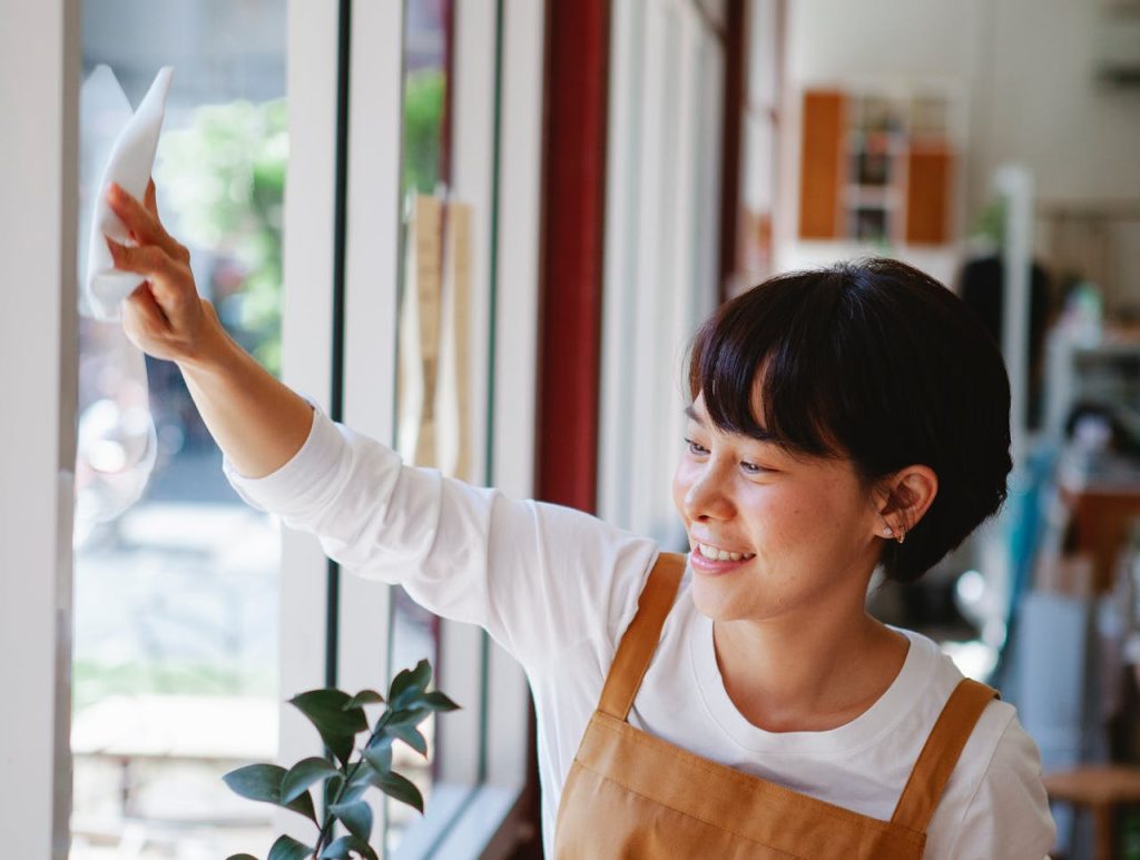 Smiling woman in apron wipes glass window at a small business. Indoor shot.